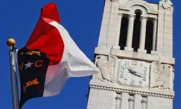 The State of NC flag flying in front of the NC State Memorial Belltower